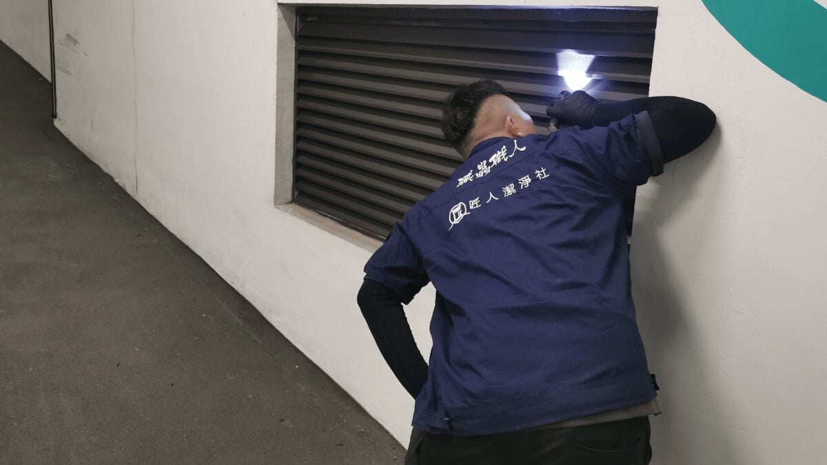 穿著藍色夾克的人在室內用手電筒檢查通風口。