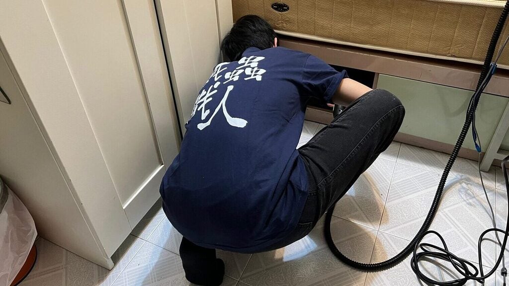 滅蟲技術員正在床底進行床蝨檢查與處理,穿著印有「滅蟲職人」制服,手持高溫蒸氣設備執行工作。