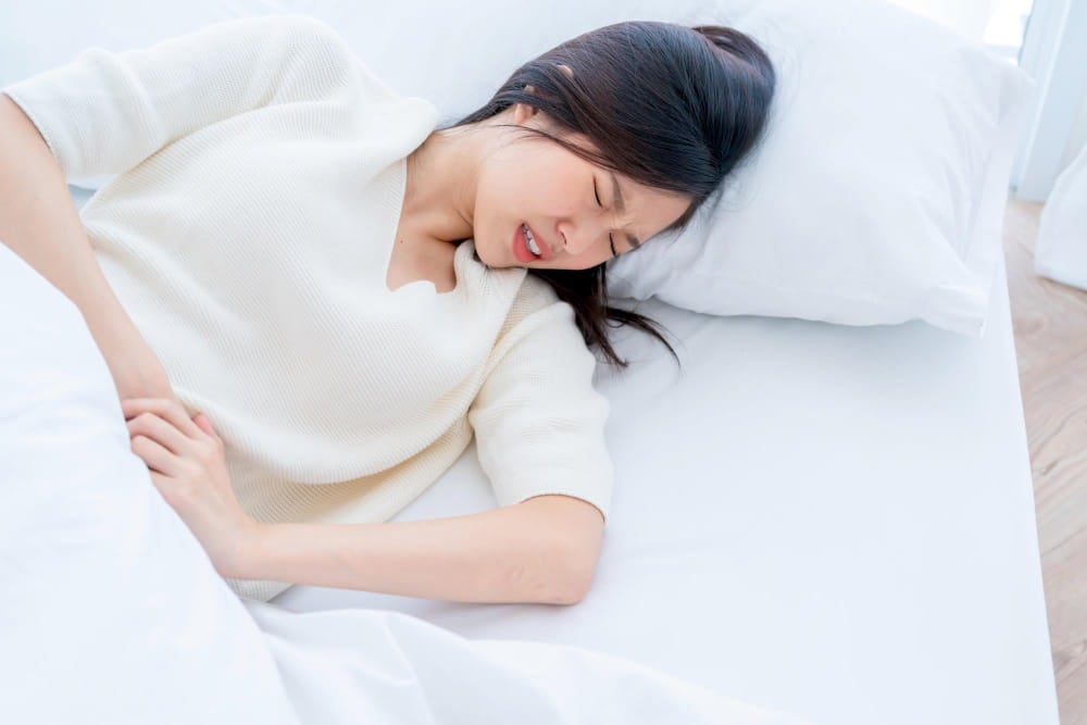 香港女士躺在床上抱腹痛苦,疑因曱甴或曱甴屎引致腸胃不適,常見於本地家庭除蟲問題.